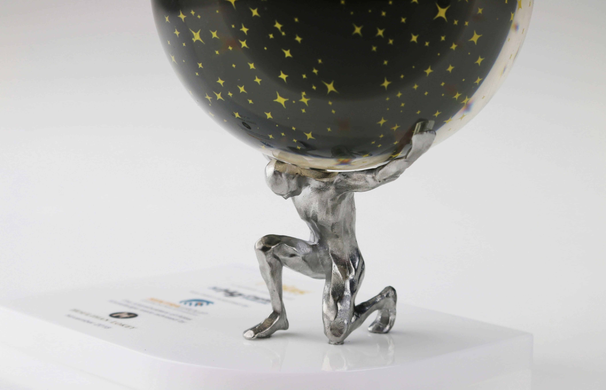 metal human figure on one knee holding a globe deal toys on his shoulder