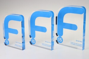 Three transparent acrylic recognition awards with blue accents, displaying numerical milestones (5, 10, 15) and recipient names.