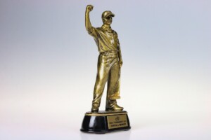 A golden recognition award featuring a figure of a man with one arm raised in a victorious pose, mounted on a black base with a plaque titled "overall winner." the background is a soft gradient from white to light grey.