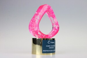 A vibrant pink acrylic recognition award with a loop design, mounted on a golden base that has a label reading "league game changer awards inspirational leader.