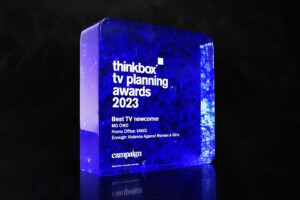 Transparent blue recognition award cube with inscription for the "thinkbox tv planning awards 2023" titled "best tv newcomer" on a dark background.