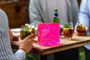 The Thinkbox TV Awards held at One Marylebone Road, 12th July 2023Photography by Fergus Burnett A vibrant pink trophy, a “thinkbox tv planning recognition awards 2023” award, prominently displayed on a wooden table surrounded by people holding glasses with drinks.