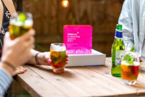 The Thinkbox TV Awards held at One Marylebone Road, 12th July 2023Photography by Fergus Burnett People enjoying drinks around a wooden table with a glowing pink "thinkbox recognition award planning & programming 2023" acrylic trophy in the center.