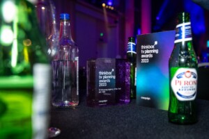 The Thinkbox TV Awards held at One Marylebone Road, 12th July 2023Photography by Fergus Burnett Close-up of event table with clear focus on a 'thinkbook ty planning recognition awards 2023' plaque, surrounded by empty glass bottles and colorful ambient lighting.