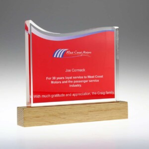 A clear acrylic recognition awards with a red and blue striped motif on top, presented to joe cormack for 30 years of service at west coast motors, mounted on a wooden base with an appreciation note from the craig family.
