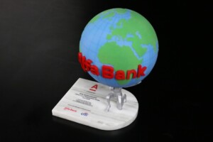 Deal toys globe, branded with "alfa-bank," stands on a white base featuring a card and miniature silver figures. one figure appears to hold the globe aloft on a dark background.