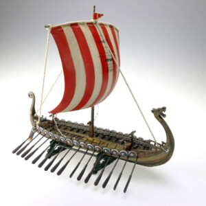 A detailed deal toys model of a viking longship with a striped red and white sail, ornate carvings, and multiple shields lining the side.