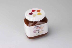 A replica jar of natra chocolate spread isolated on a plain white background, displaying a white deal toys label with colourful geometric shapes and the brand logo.