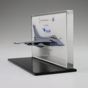 A deal toys model of a jet airplane mounted on a stand, featuring logos and text with the name "alkan" and "alnatra 2017" on a display plaque in front of a gray background.