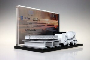 Deal toys featuring miniature steel beams, pipes, and a cement mixer truck, placed on a black base with a company logo and text on a clear backdrop.