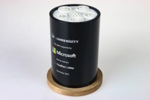 Cylindrical black deal toys with a Microsoft logo and other text, featuring a decorative pattern of white floral designs on top, displayed on a round wooden base.