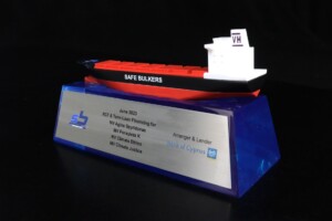 A deal toys model of a red and white ship labeled "safe bulkers" mounted on a clear blue acrylic stand with text detailing a june 2022 loan arrangement by bank of cyprus.