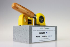 Two yellow stanley tape measures and a wooden-handle hammer positioned on a gray concrete block with a deal toys plaque on the front.