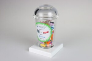 A clear plastic container filled with colorful paper clips on a white pedestal, featuring a deal toys label that includes logos for "a&m capital europe" and "bonito group".