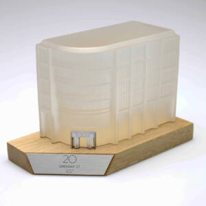 Scale model of a building encased in translucent acrylic, with a labeled wooden base stating "20 gresham st". the deal toys include detailed windows and a small cube marking the address.