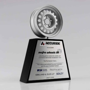 A silver wheel on a black base with financial tombstones text and logo on a metal plate