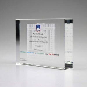 Transparent financial tombstones with details of a bond issuance for the republic of slovenia, including logos of involved banks, displayed on a reflective gray surface.