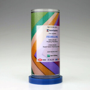 Cylindrical financial tombstones featuring a colorful geometric design with text announcing the acquisition of fedrigoni by baincapital, including financial details and logos of joint bookrunners.