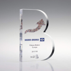 Transparent acrylic financial tombstones shaped like a letter "b" with a colorful crowd silhouette and text "knorr-bremse fitness brakes europe 2017/18" on a gray background.