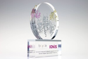 Transparent crystal financial tombstones with a circular top illustrating a colorful molecular structure, mounted on a base that features the logos for "ionis" and "bryvle therapeutics.