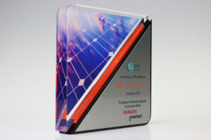 Clear acrylic financial tombstones with a solar panel design, a red side accent, and inscriptions detailing an acquisition event and advisors involved, set against a light grey background.