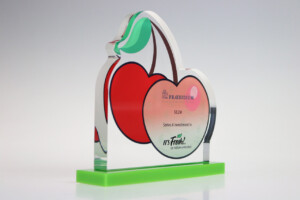 Transparent acrylic financial tombstones with a colorful design of two cherries and green leaves on top. it displays text about a $32m series a investment for "praesidium." the base is neon green.