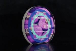 Acrylic financial tombstones with colorful graphics displaying various company logos and text commemorating a business acquisition, showcased against a dark background.