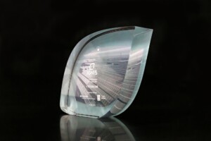 Transparent acrylic financial tombstones with a frosted logo and text detailing an achievement, displayed against a dark reflective background.