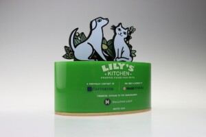 Financial tombstones for lily's kitchen featuring a green fondant base with printed logos of related corporations and a top decoration of two cartoon animals surrounded by leaves.