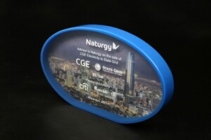 Oval-shaped, blue acrylic tombstones featuring the naturgy logo with details about advising on a $1.6 billion sale to state grid. background image shows a city skyline.