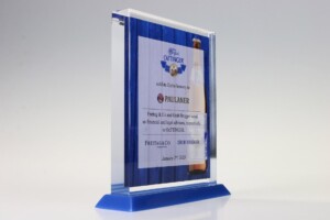 Clear acrylic financial tombstones with blue accents, featuring a printed design with logos, a beer bottle image, and text commemorating an achievement, set against a white background.