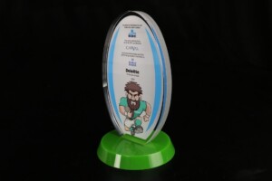 Rugby ball shaped financial tombstones with a cartoon illustration of a man running, mounted on a green base, bearing logos of kbc, cavay, and deloitte, and text acknowledging outstanding effort.