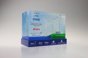 Transparent acrylic financial tombstones featuring a design with wind turbines and solar panels, with logos of e.on and other sponsors, celebrating renewable energy achievements.