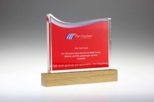 A translucent rectangular award with curved red accents on a wooden base, engraved with a personal dedication to joe cormack for 30 years of service at west coast motors.