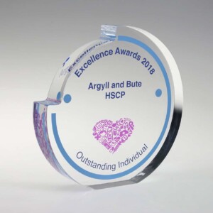 A circular glass recognition award with beveled edges, engraved with "excellence awards 2018 - argyll and bute hscp, outstanding individual," featuring a detailed emblem at the bottom.